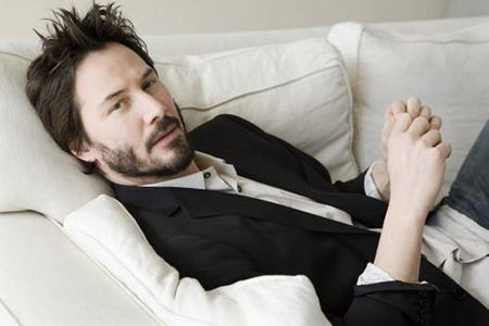 Keanu lies on a couch as he poses for the camera.